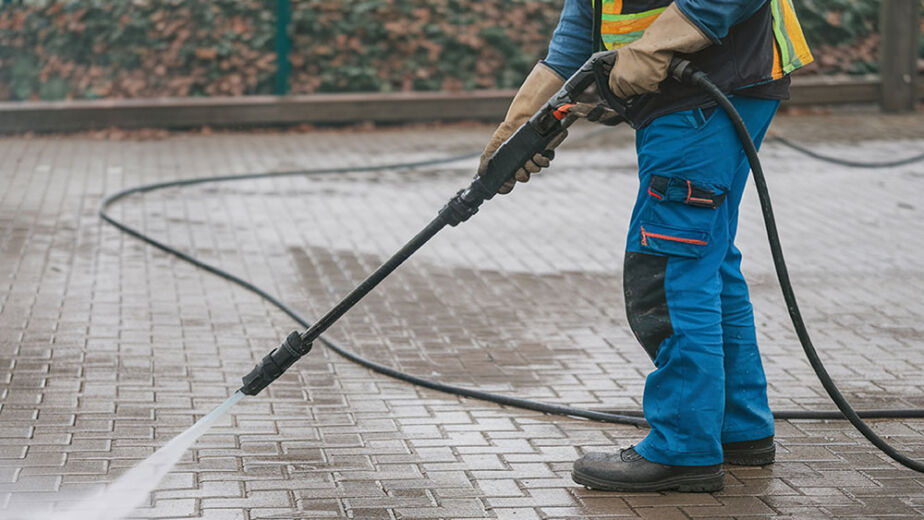 A man with a gun is spraying water on a brick sidewalk