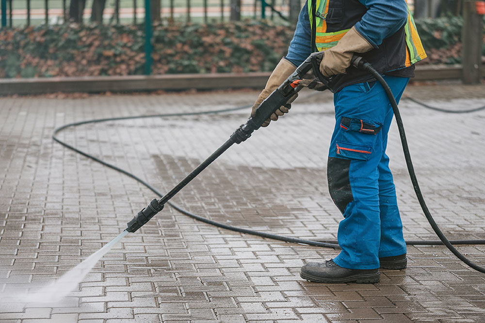 A man with a gun is spraying water on a brick sidewalk